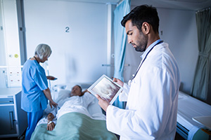 Arzt schaut auf ein medizinisches Tablet, während eine Krankenschwester einem Patienten im Krankenhaus hilft