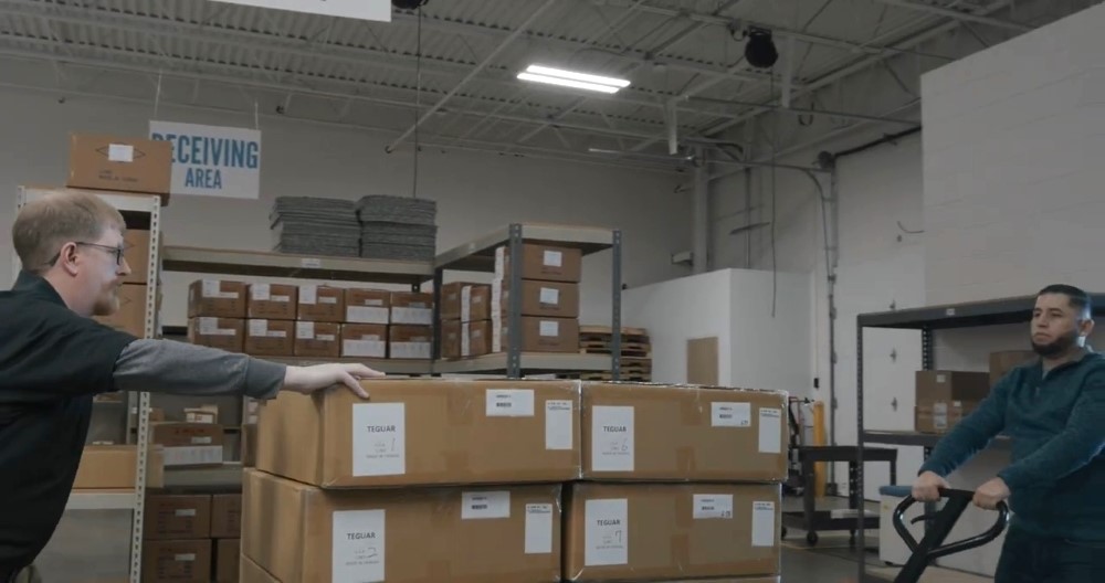 Two Teguar employees push a pallet of boxed Teguar products through their warehouse to load onto a truck for shipment. 