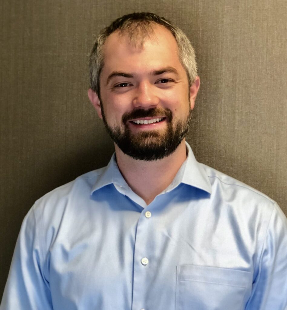 Bryce Keeney lächelt in einem hellblauen Hemd mit Kragen in die Kamera.