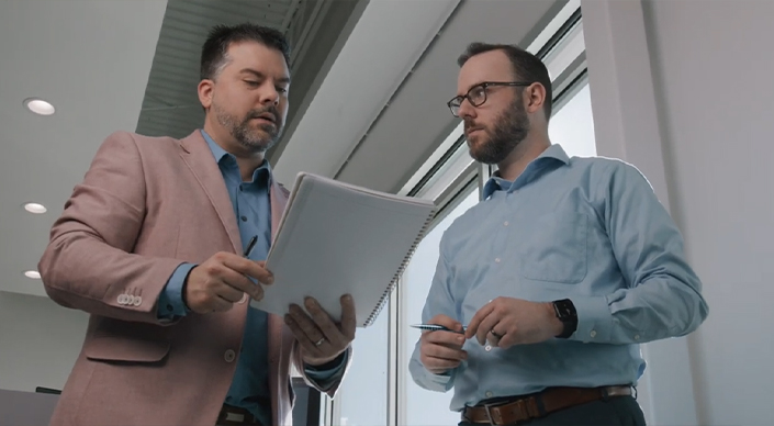 Two Teguar team members discuss ideas over a notebook.