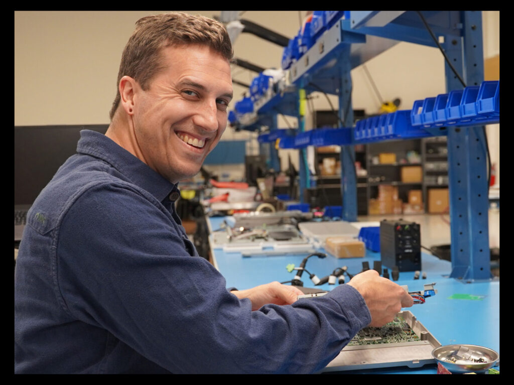 Teguar-Techniker lächelt in die Kamera, während er an einem Computer arbeitet