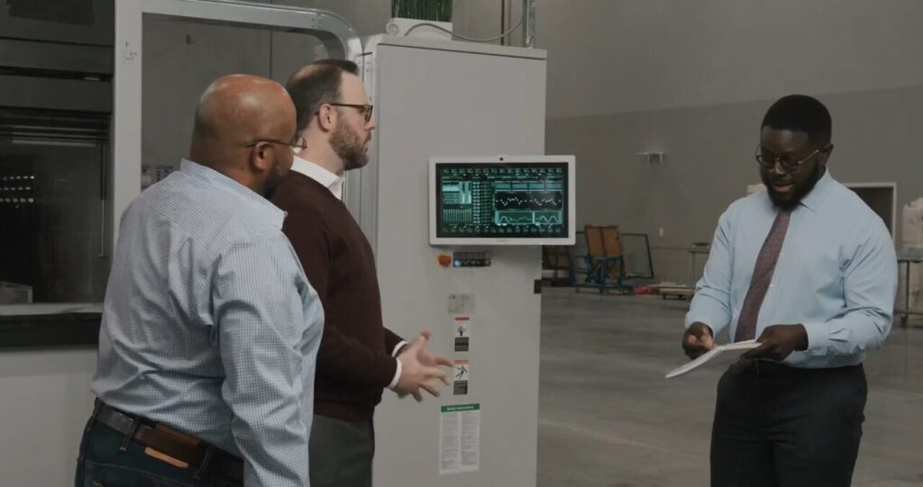 Vertreter von Teguar sehen sich mit ihrem Kunden einen an der Wand montierten Panel-Computer an.  