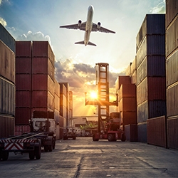 Commercial airplane flies over a shipyard full of containers