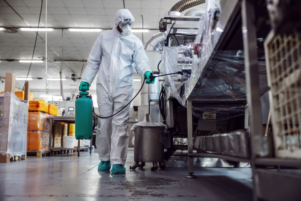 Person in clean room attire spraying down factory equipment for sanitization