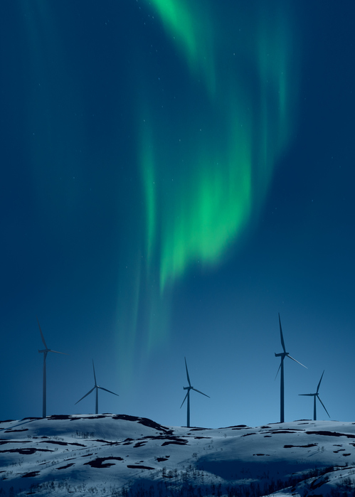 Northern light above wind turbines on snowy hill in winter night