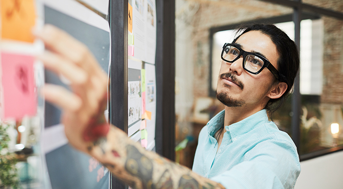 A man reaches toward a note posted on a project board.