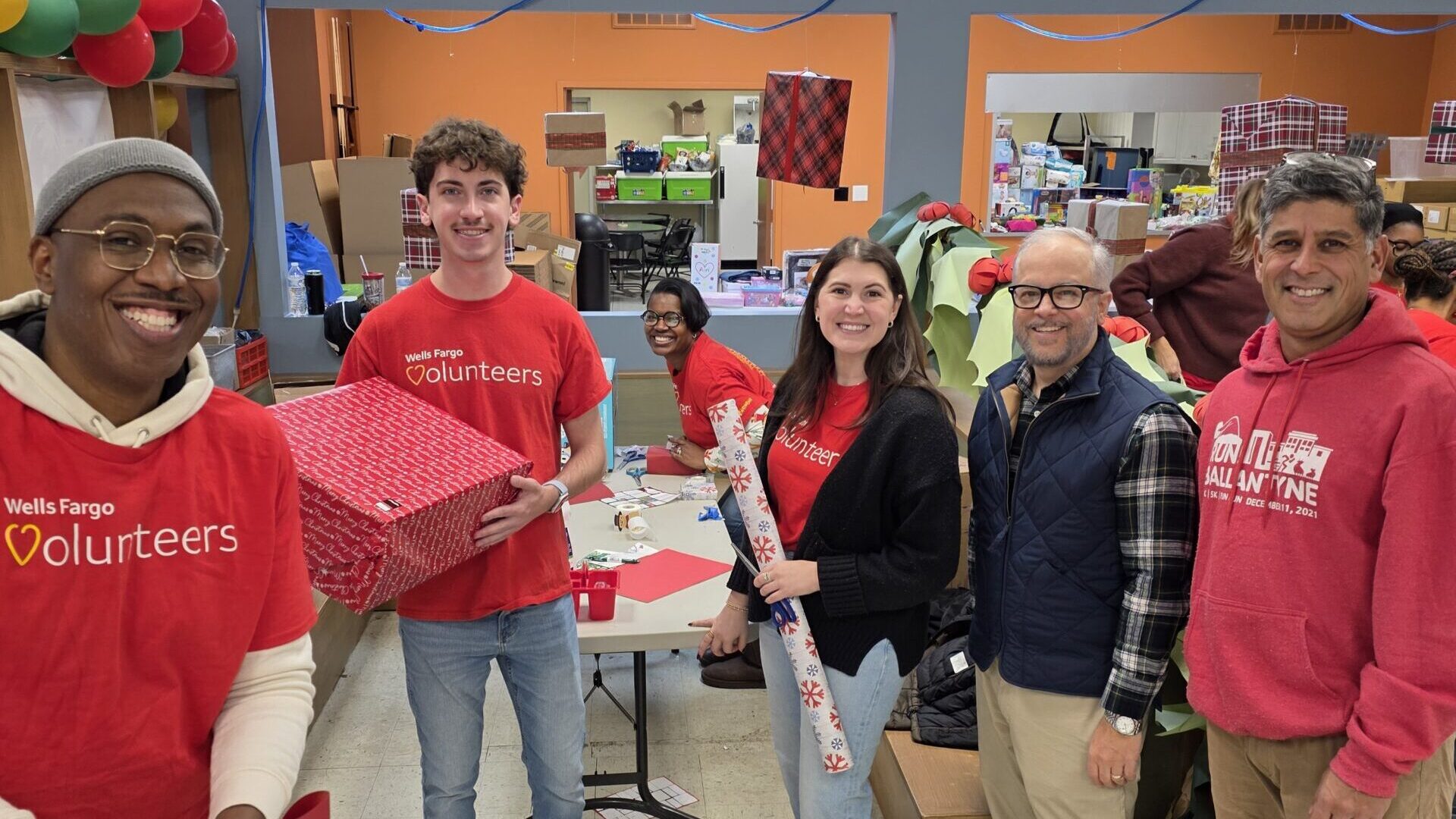 HopeMATCH volunteers standing in a cheerily decorated room holding gift wrapping and gifts.