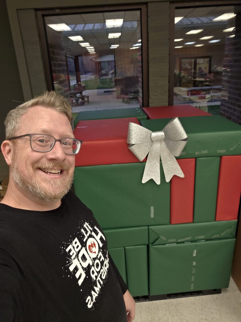HopeMATCH volunteer smiles with a large stack of wrapped gift boxes.