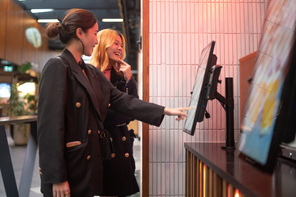 Two friends ordering a meal on touch screen kiosk